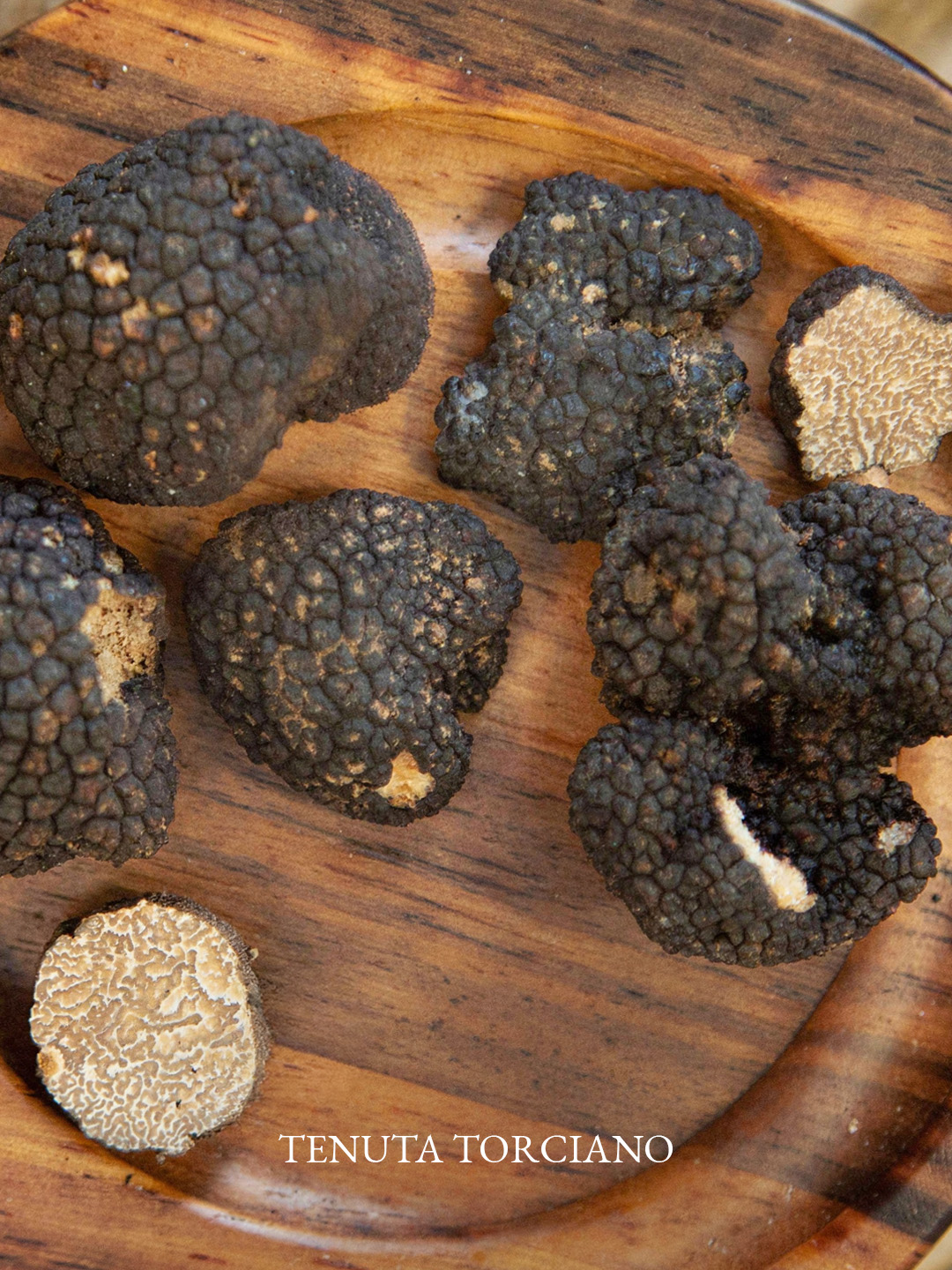 Tartufi neri freschi e un tartufo tagliato su un tagliere di legno a Tenuta Torciano
