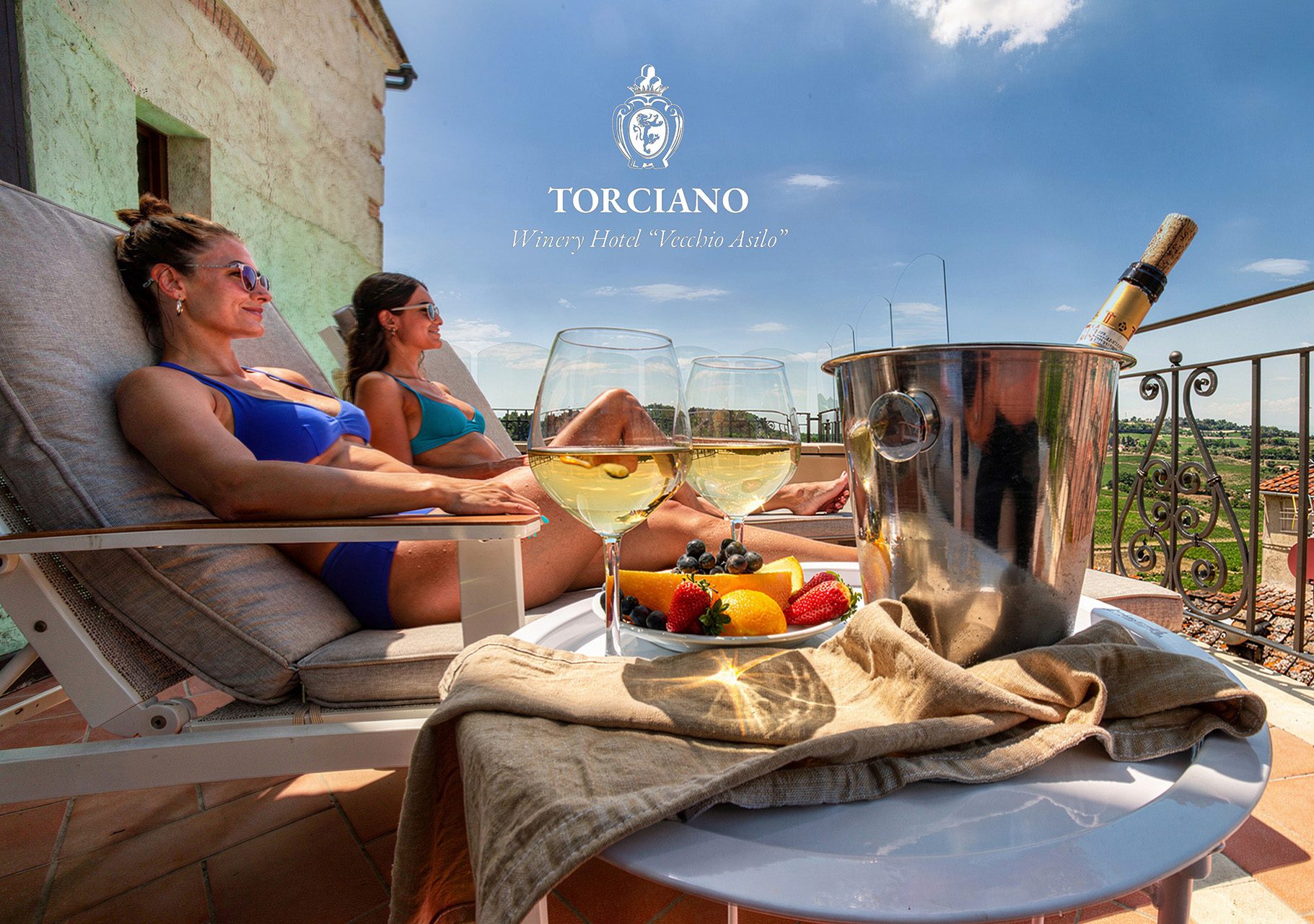 Two guests relaxing on the terrace of Hotel Torciano Vecchio Asilo with chilled white wine, fruit and the Tuscan hills beyond