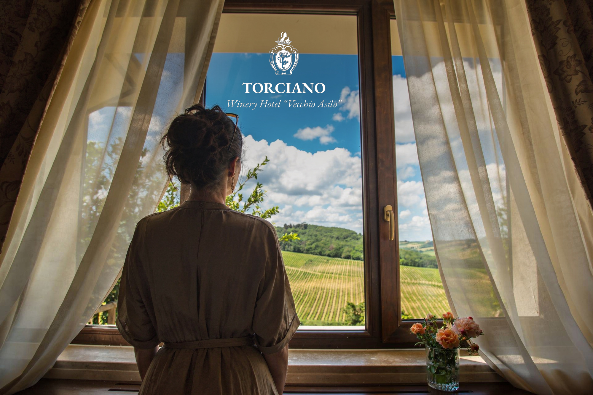 Un'ospite affacciata alla finestra della camera guarda i filari e le colline dall'Hotel Torciano &laquo;Vecchio Asilo&raquo;