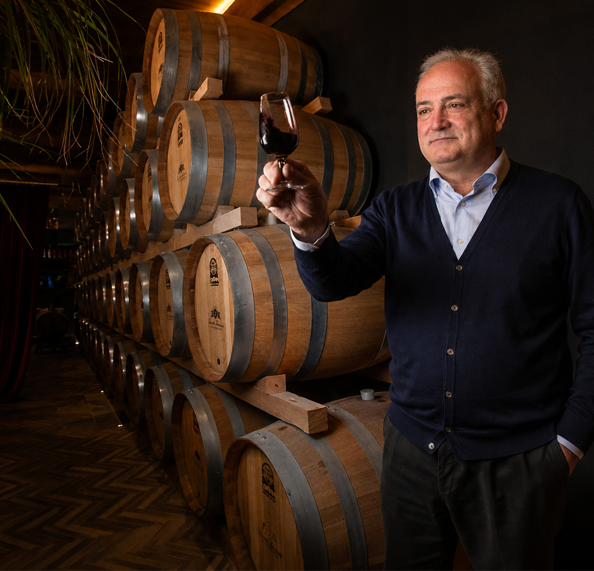 The Torciano winemaker raising a glass of red wine beside the stacked oak barrels of the estate cellar
