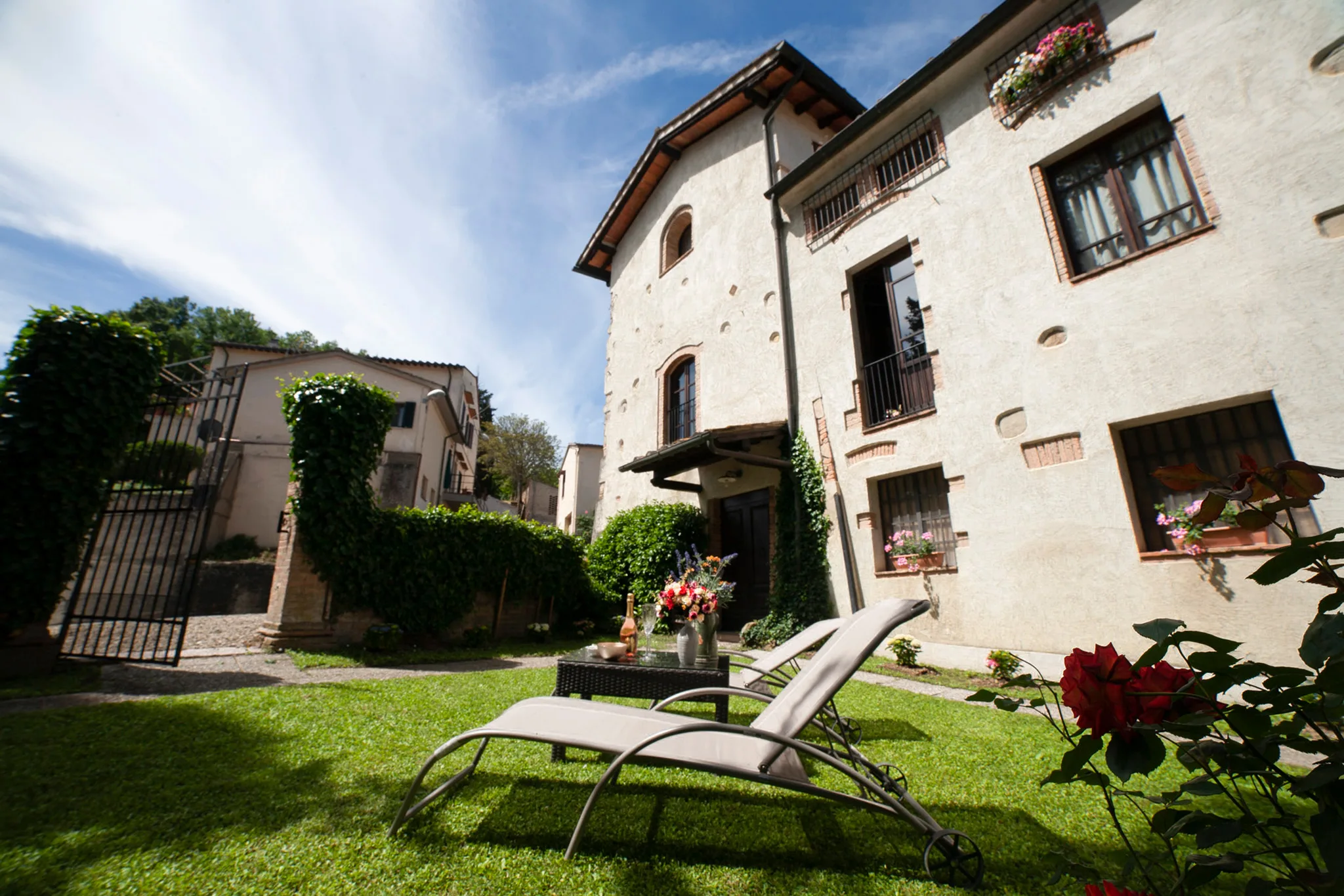 Il giardino di Hotel Torciano Vecchio Asilo al mattino, con lettini e una bottiglia di vino Torciano sul prato